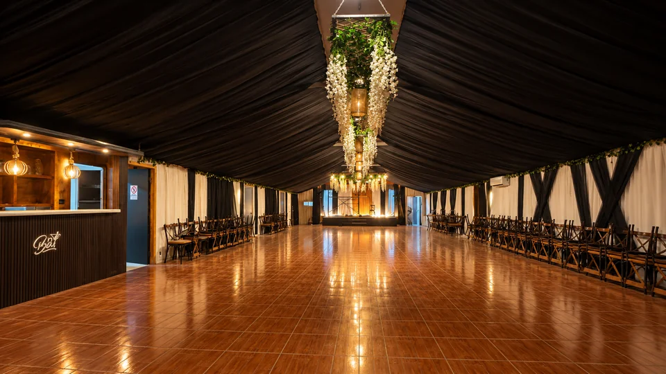 Salón sin montaje de mesas, con piso despejado y escenario al fondo